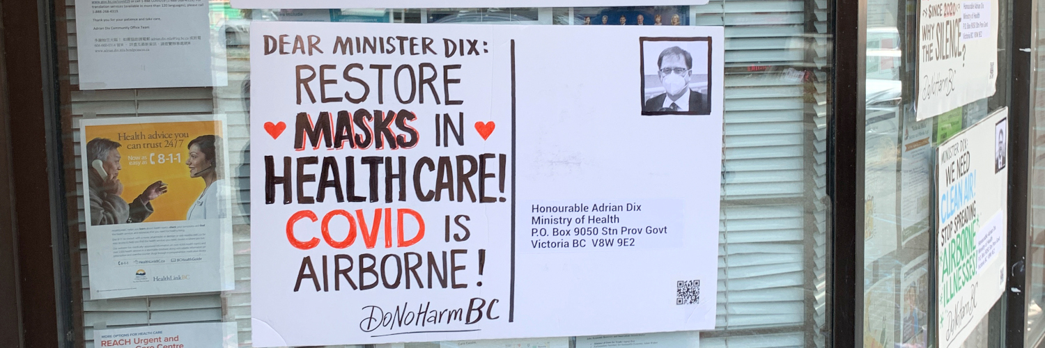 An oversized postcard affixed to the window of Adrian Dix’s MLA office. The postcard reads, “Dear Minister Dix: Restore Masks in Healthcare! Covid is Airborne! DoNoHarm BC.” In place of a postage stamp is a headshot of Health Minister Adrian Dix wearing a respirator mask. Photo from DoNoHarm BC.