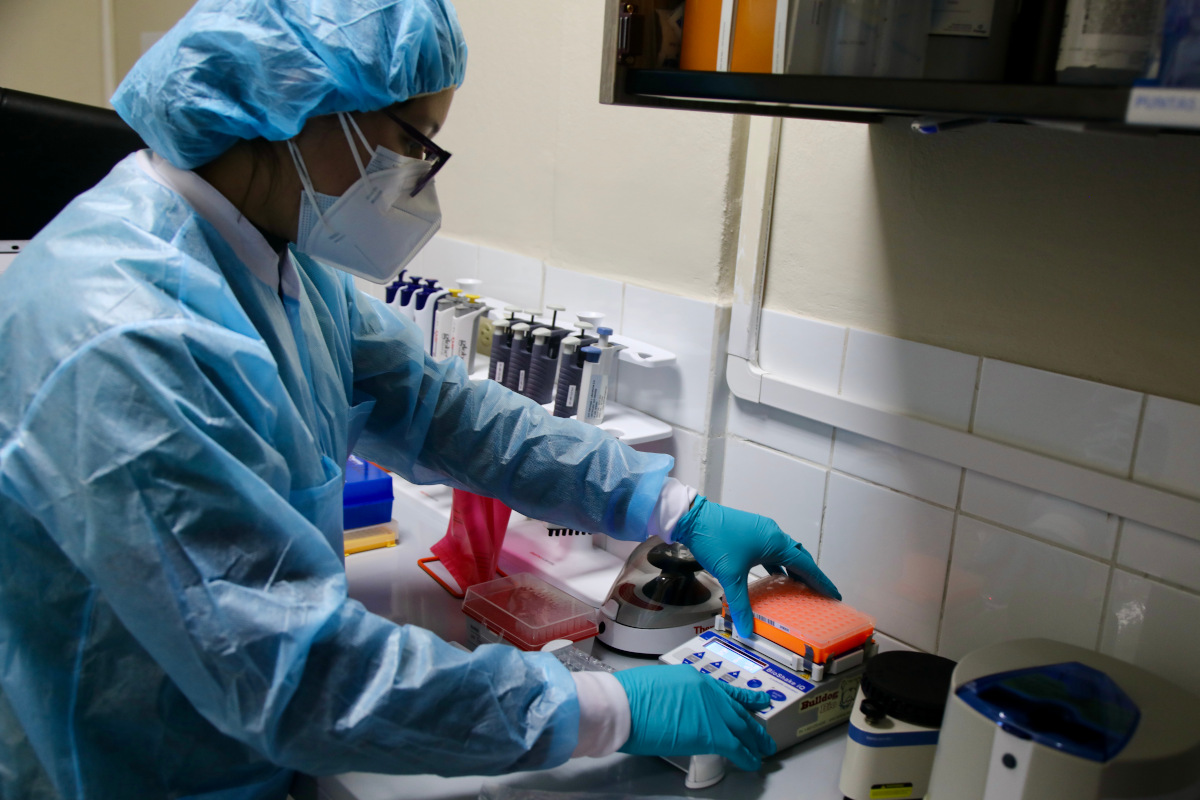 A healthcare worker conducts genomic sequencing of the SARS-COV-2 virus at the National Virology Laboratory in Honduras, on March 29, 2023. The healthcare worker is wearing a light blue translucent protective gown and cap, teal blue gloves, and a white respirator. Photo by: Pan-American Health Organization (PAHO) / World Health Organization (WHO).