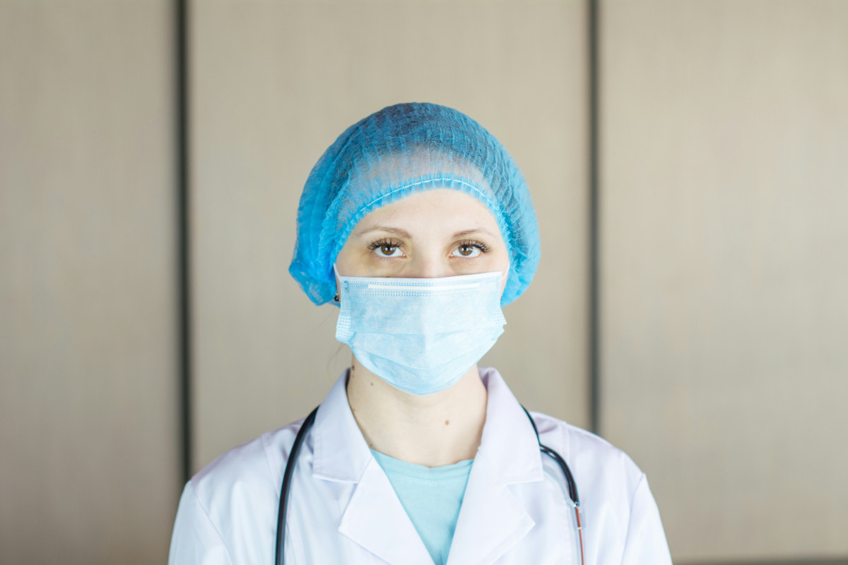 Photo of a doctor. She is wearing an obsolete blue medical mask, a blue cap and a white gown. Photo: Bermix Studio / Unsplash.