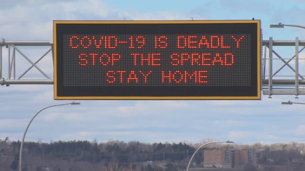 Photo d’un panneau au-dessus d’une autoroute avec un texte rouge majuscule sur un fond gris charbon de bois qui se lit comme suit : « COVID-19 est mortel arrêter la propagation rester à la maison ».